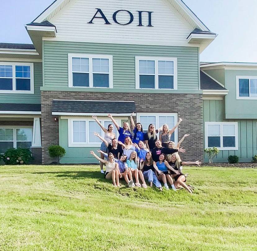 Members of Alpha Omicron Pi standing in front of the sorority house
